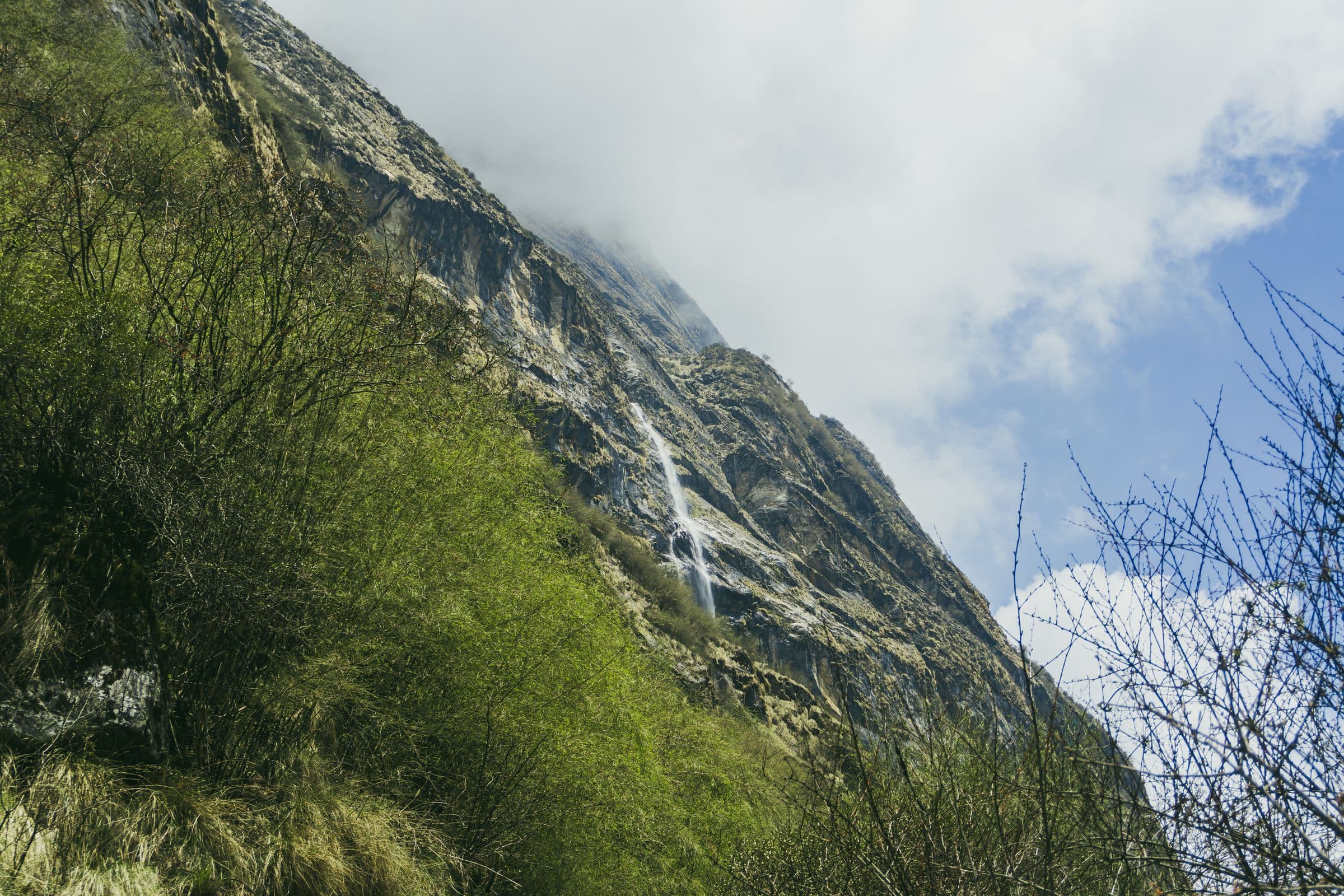Beautiful waterfall cascading down a mountainside in Ghandruk, Nepal, surrounded by lush greenery.