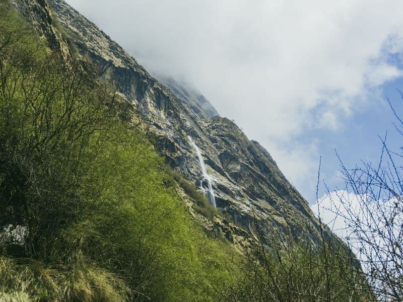 Beautiful waterfall cascading down a mountainside in Ghandruk, Nepal, surrounded by lush greenery.