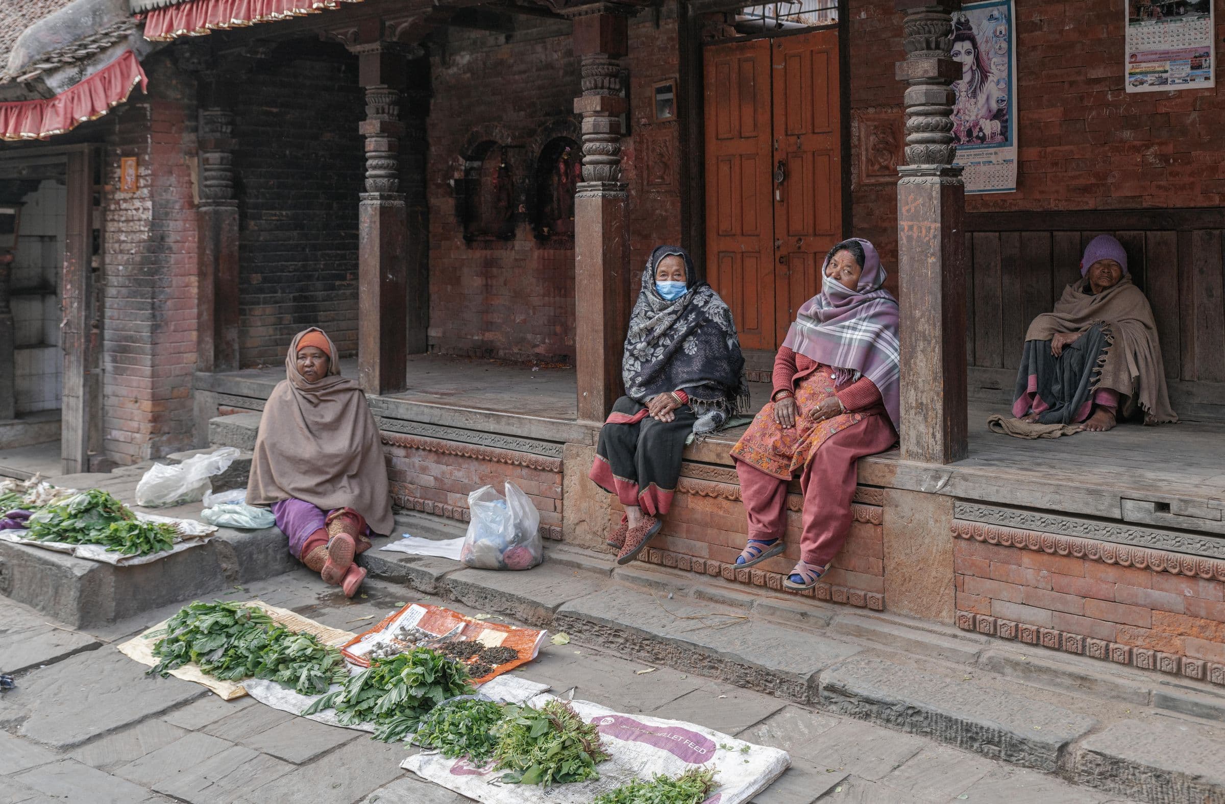 Four women in traditional clothing at a street market in Bhaktapur, Nepal, selling fresh produce.