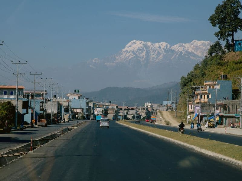 A tranquil view of a road leading to the Himalayas with snow-capped peaks in the background.