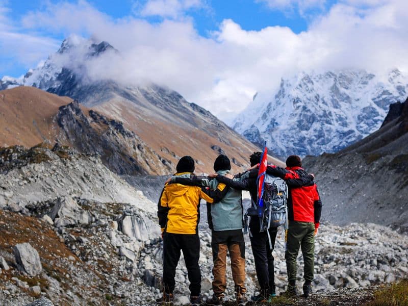 Four hikers stand arm in arm, embracing the majestic snowcapped mountain landscape.