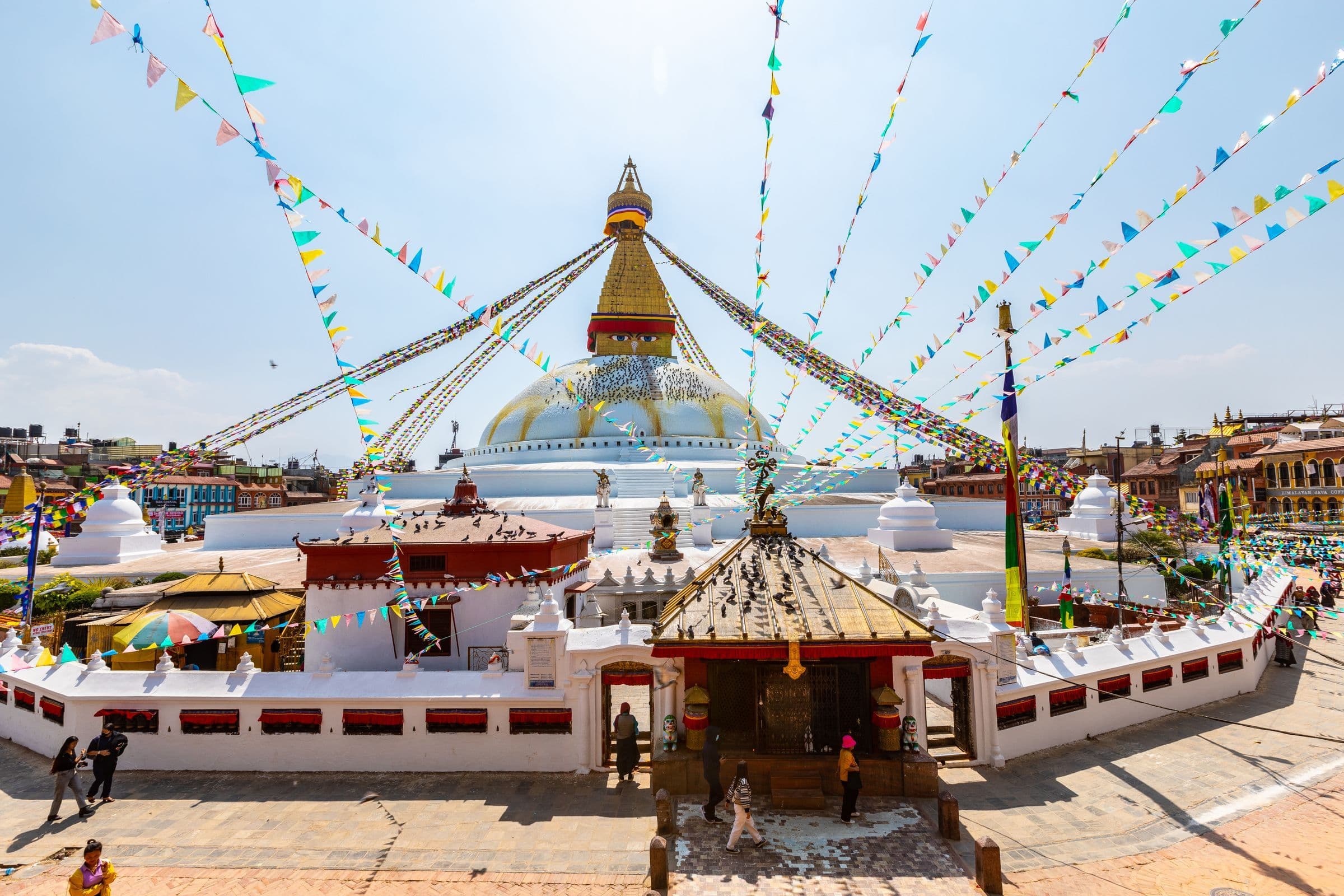 Vibrant scene of Boudhanath Stupa in Kathmandu, Nepal, adorned with colorful prayer flags and bustling with tourists.