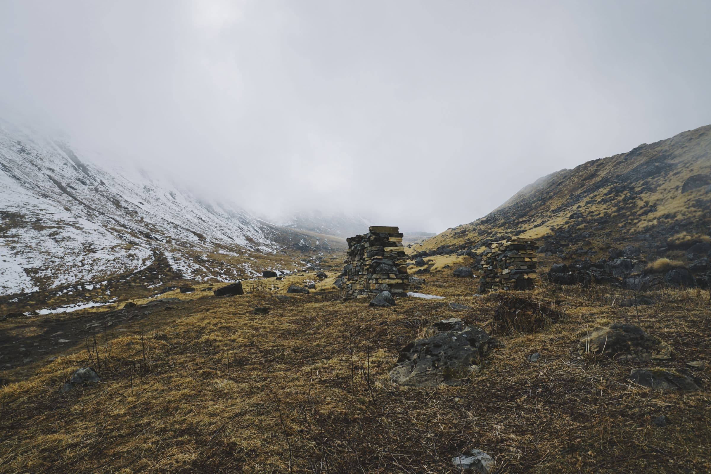 Explore the serene, snow-dusted mountains of Ghandruk, Nepal, featuring piled stones and misty skies.
