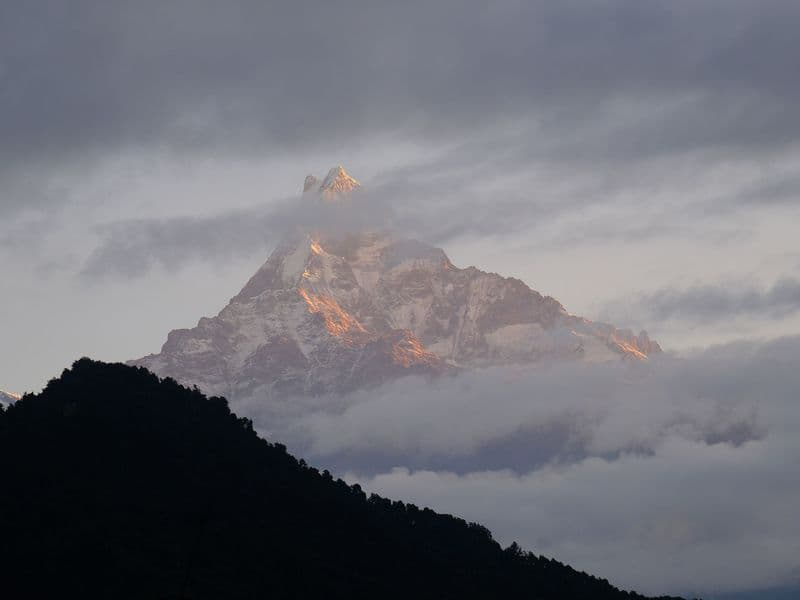 Scenic view of a mountain peak above clouds at sunrise in serene landscape.