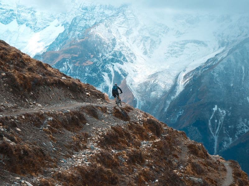 Cyclist on rugged mountain trail in Khangsar, Nepal with snow-capped peaks.