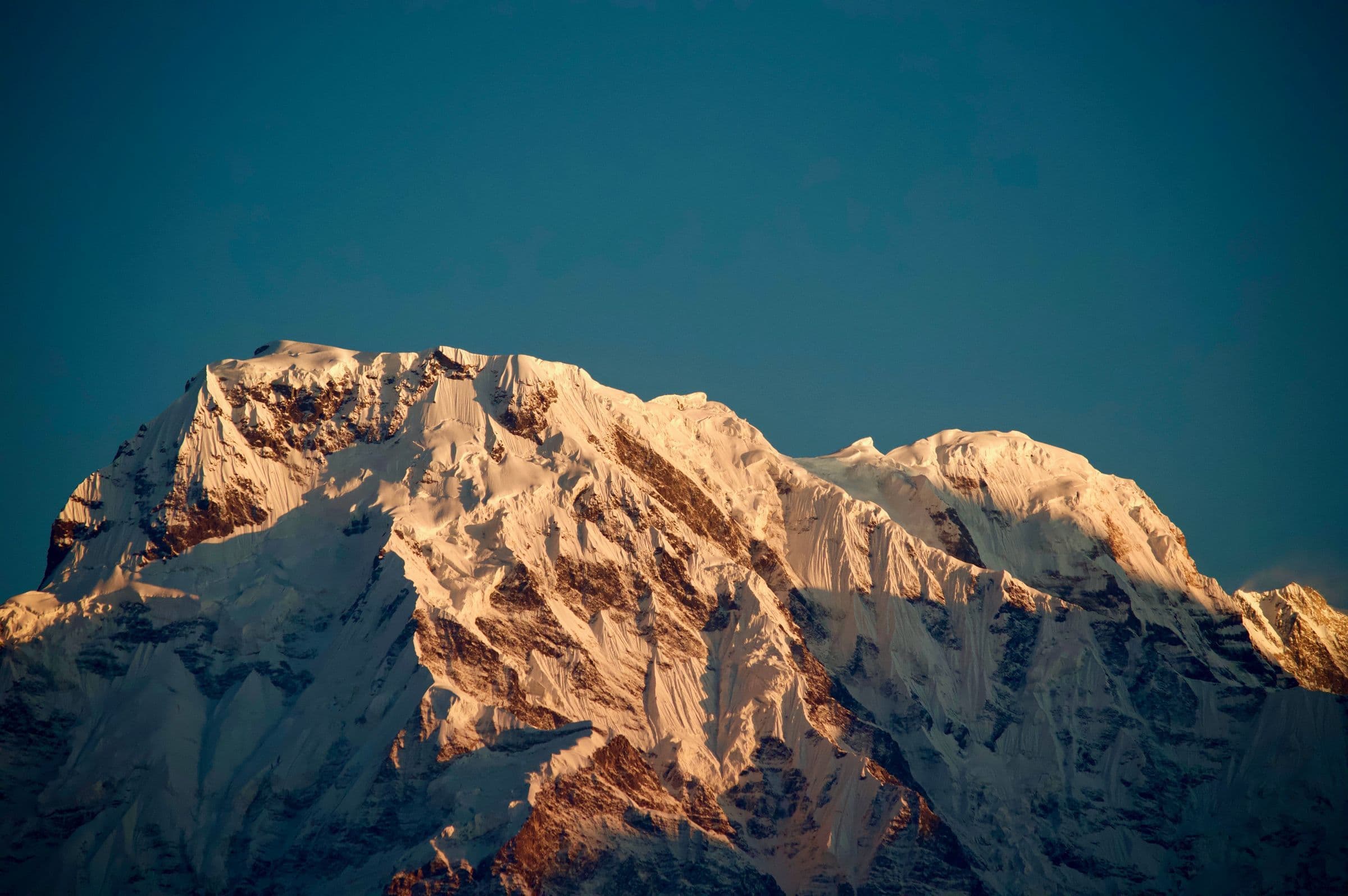 A stunning view of a snow-capped mountain peak illuminated by sunrise light, capturing nature's beauty.