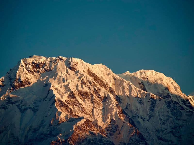 A stunning view of a snow-capped mountain peak illuminated by sunrise light, capturing nature's beauty.