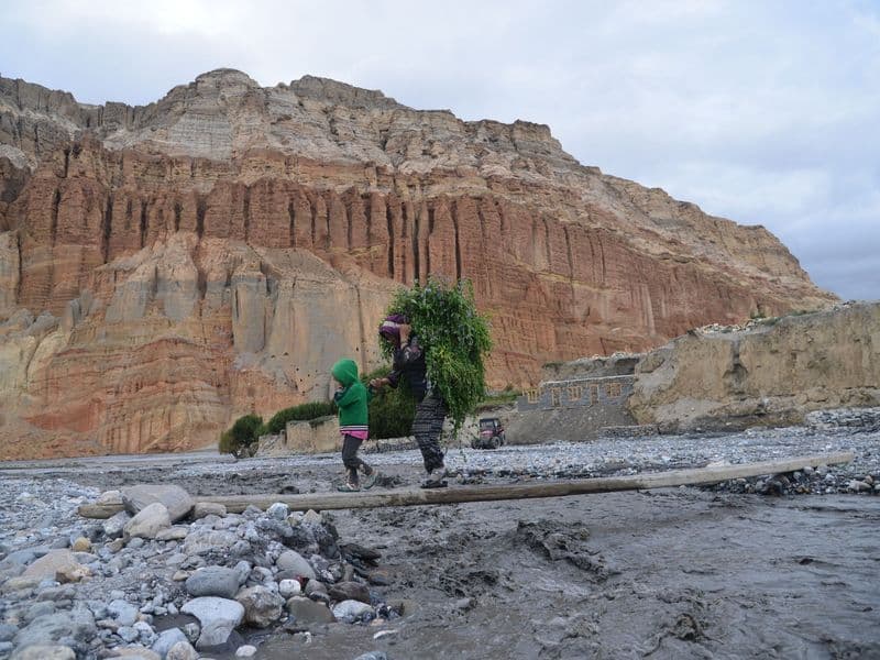 A mother and child walk across a rocky landscape in Upper Mustang, Nepal with a steep cliff backdrop.