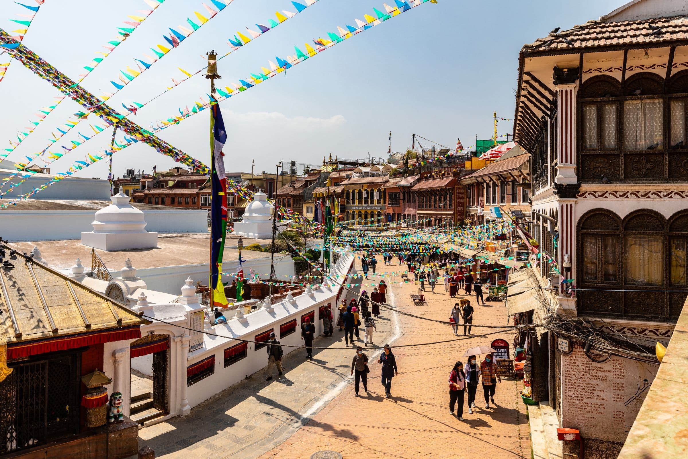 Colorful flags and lively streets around Boudhanath Stupa in Kathmandu, Nepal, with bustling activity.