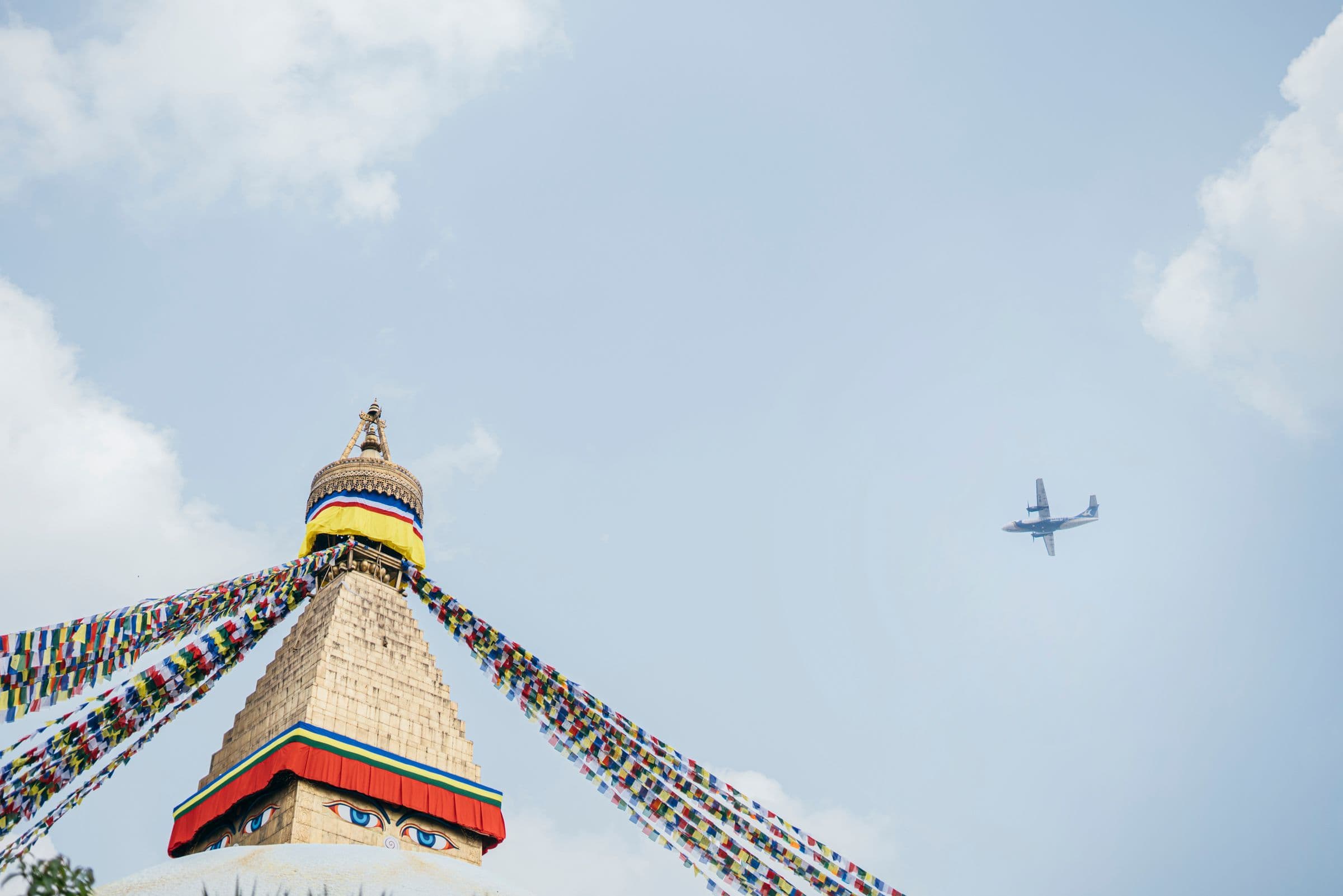 Boudhanath Stupa in Kathmandu, Nepal with vibrant prayer flags and an airplane in the sky.