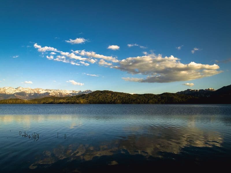 Serene view of Rara Lake with clear blue skies and reflections, surrounded by mountains in Nepal.