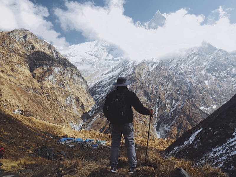 A lone hiker stands with trekking poles, admiring the breathtaking Himalayas in Nepal.